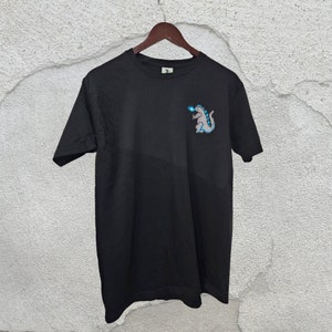 May include: Black t-shirt with a graphic of a gray monster with blue flames on the left chest.