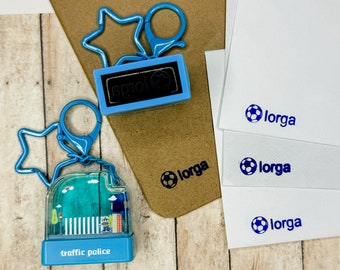 Puede incluir: Colección de llaveros azules y artículos de papelería. Un llavero tiene forma de estrella, el otro es una bola de nieve en miniatura con una escena de policía de tráfico. Papel blanco con un logotipo de balón de fútbol azul y la palabra "lorga".