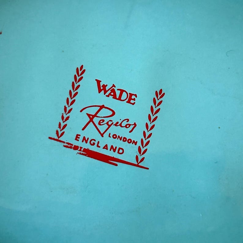 May include: A close-up of a light blue surface with a red logo. The logo reads "Wade Regicor London England" with decorative elements. The text is in a stylized font.
