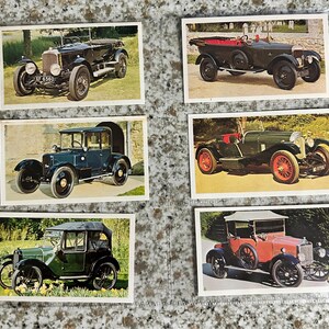 May include: Six vintage car trading cards. The cards feature classic cars in various colors, including black, green, and red. The cars are shown in outdoor settings, with details like headlights and wheels visible.