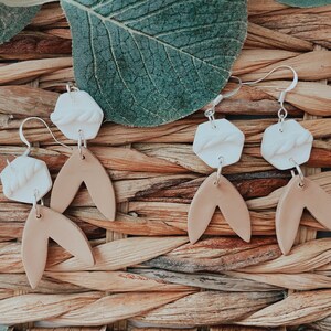 May include: A pair of dangle earrings with white hexagonal clay charms and brown clay leaf-shaped charms. The charms are connected by silver jump rings and silver hooks.
