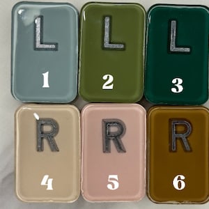 Op de afbeelding: Zes vierkante tegels met afgeronde hoeken, elk met een letter en een nummer. De tegels zijn in verschillende kleuren: lichtblauw, groen, donkergroen, beige, roze en bruin. De letters zijn L en R, en de nummers zijn 1 tot en met 6.