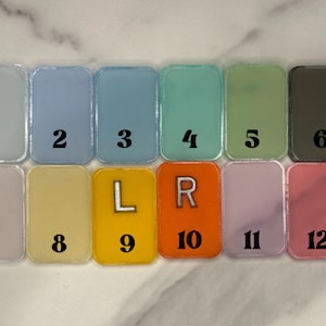 May include: Twelve small, rectangular tiles with rounded corners. Each tile has a different colour and a number from 1 to 12. Tiles 9 and 10 have letters L and R instead of numbers.