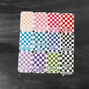 Op de afbeelding: Een set van 10 kleine, vierkante blikjes met een schaakbordpatroon in verschillende kleuren. De blikjes zijn gelabeld met de kleuren: Perzik, Roze, Heet roze, Rood, Lichtblauw, Caribisch blauw, Blauw, Zwart, Lila, Paars, Groen, Donkergroen.