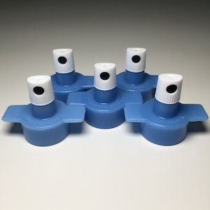 May include: Five blue plastic bottle caps with white tops and black centers. The caps have a small wing on each side.