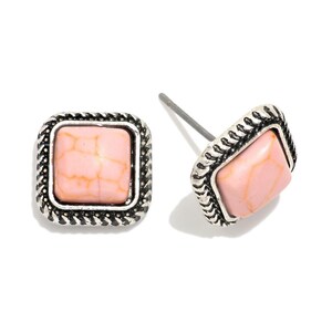 May include: A pair of square stud earrings. Each earring features a light pink, textured stone set within a silver-toned, braided frame. The earrings are displayed on a white background.