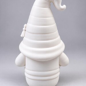 Back view of the white unpainted gnome figurine, showing the ridges of its large pointed hat and round body against a neutral gray background.