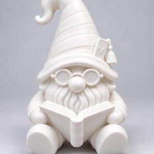 Front view of the white unpainted gnome figurine holding an open book, wearing a pointed hat with a tassel and round glasses, against a plain gray background.