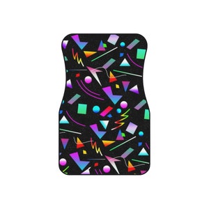 Op de afbeelding: Een zwarte autovloermat met een geometrisch patroon in neonkleuren, waaronder roze, blauw, groen en geel.