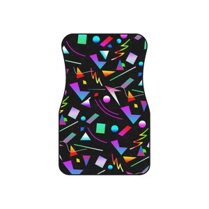 Op de afbeelding: Een zwarte autovloermat met een geometrisch patroon in felle kleuren, waaronder roze, blauw, groen, geel en oranje. Het patroon doet denken aan het ontwerp uit de jaren 80 en 90.