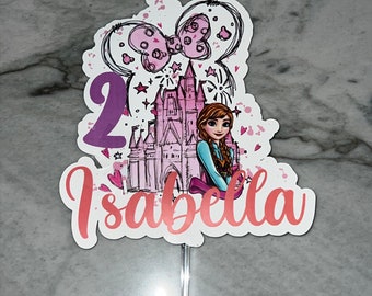 Può includere: Decorazione per torta con un'illustrazione di principessa, un castello e il numero 2. Il nome "Isabella" è scritto in rosa. Il design include un fiocco e stelle. Fissato a un bastoncino d'argento.
