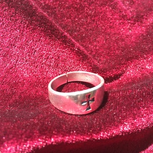 Puede incluir: Un anillo de plata con un diseño de cruz sobre un fondo de terciopelo rojo.