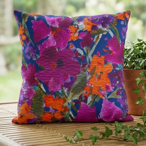 Almofada de jardim externa pintada de azul, com flores em aquarela rosa, laranja e roxa.