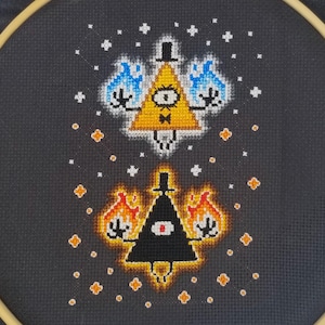 Könnte beinhalten: Eine schwarze und weiße Kreuzstich-Stickerei mit zwei Dreiecken mit Augen, eines gelb mit blauen Flammen und das andere schwarz mit orangefarbenen Flammen, auf einem dunkelgrauen Hintergrund mit weißen Sternen.