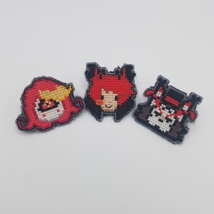 May include: Three embroidered patches featuring characters from the animated series "Hazbin Hotel". The patches are red, black, and white with pixelated designs.