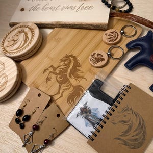 May include: A collection of horse-themed items, including wooden coasters, keychains, a cutting board, earrings, a notebook, and a leather star. The items are in shades of brown, black, and silver. A wooden sign with the text "Where the dust flies & the heart runs free" is also present.