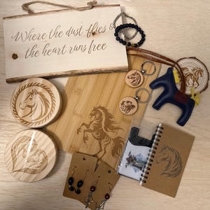 May include: A collection of horse-themed items, including a wooden sign with text, coasters, keychains, a cutting board, a leather horse figurine, earrings, a bracelet, and a notebook. The items are in shades of brown, black, and blue.