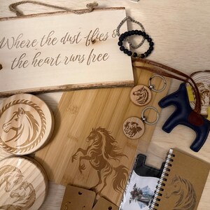 May include: A collection of horse-themed items, including a wooden sign with text, coasters, keychains, a cutting board, a leather horse figurine, a notebook, and bracelets. The items are in shades of brown, beige, and blue.