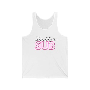 May include: White vest top featuring the text "Daddy's SUB" in black script and pink block letters. The sleeveless top has a scoop neck and is made of a soft material.