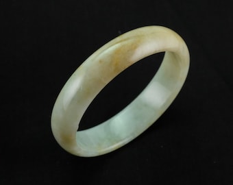 May include: A light green jade bangle with a subtle yellow hue. The bangle is smooth and polished, with a slightly rounded shape.