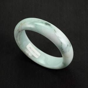May include: A light green jade bangle bracelet with a white and green marbled pattern. The bracelet has a sticker on the inside with the number "801158031049".