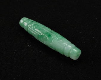 Puede incluir: Un colgante de jade verde tallado con intrincados detalles. El colgante es liso y pulido, con forma cilíndrica.
