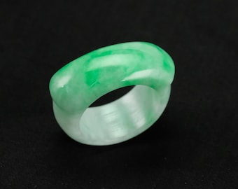 May include: A jade ring with a smooth, polished surface. The ring features a blend of light green and white hues, creating a marbled effect. The ring is a solid band, showcasing the natural variations in the stone.