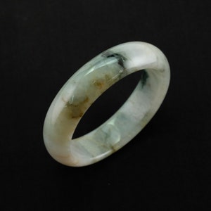May include: A jade bangle bracelet with a light green and white color scheme. The bangle is smooth and polished, with a slightly oval shape.