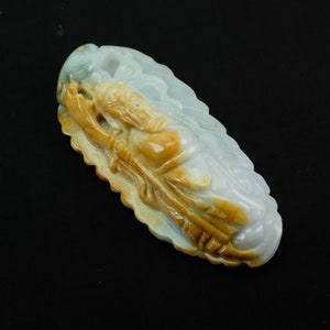 Pode incluir: Um pingente de jade esculpido com a figura de uma pessoa segurando um cajado, com um esquema de cores verde e amarelo.