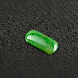 Op de afbeelding: Een gladde, groene jade-steen met een licht afgeronde rechthoekige vorm.