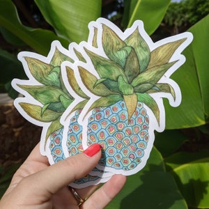 Op de afbeelding: Drie gelaagde stickers van een ananas met een blauwe en gele gepatenteerde schil en groene bladeren.