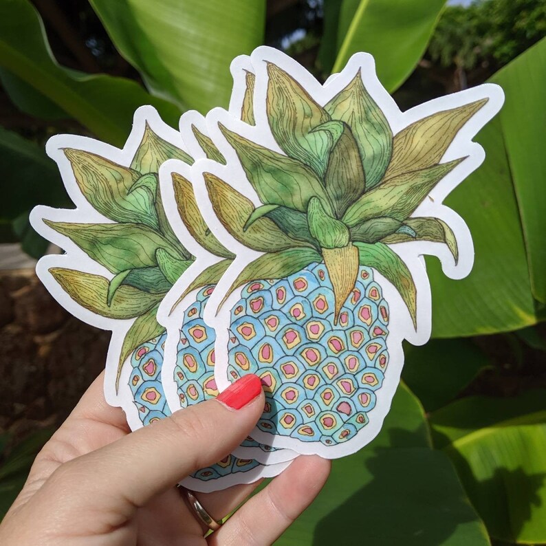 Op de afbeelding: Drie gelaagde stickers van een ananas met een blauwe en gele gepatenteerde schil en groene bladeren.