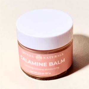 May include: A jar of Calamine Balm by Arvyda Naturals. The jar has a white lid and a pink label with the product name and description. The net weight is 2.0 oz / 57 g.
