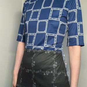 May include: A blue top with a white geometric pattern and short sleeves. The top is paired with a black skirt-like garment with a floral design.