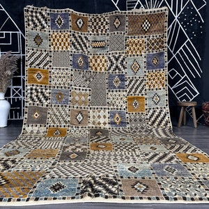 May include: A large, rectangular rug with a patchwork design. The rug is made up of squares of different colors and patterns, including brown, beige, blue, and black. The rug has a fringe border.