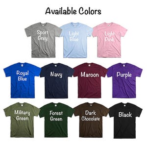 Może przedstawiać: Kolekcja koszulek w r&oacute;żnych kolorach, w tym Sport Grey, Light Blue, Light Pink, Royal Blue, Navy, Maroon, Purple, Military Green, Forest Green, Dark Chocolate i Black. Każda koszulka wyświetla nazwę koloru białym tekstem.