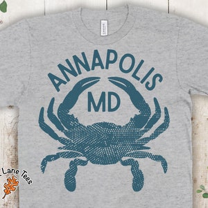 May include: A grey t-shirt with a blue crab design and the text "ANNAPOLIS MD" printed on the front.