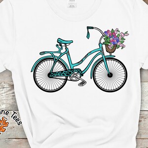 Puede incluir: Una bicicleta turquesa con una cesta de flores en el manillar. La bicicleta tiene un fondo blanco.