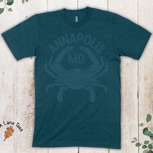 May include: Teal blue t-shirt with a distressed white graphic of a crab with the text "ANNAPOLIS MD" above it.