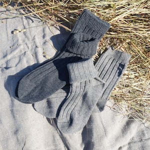 May include: A pair of dark charcoal gray ribbed knit socks and a pair of light heather gray ribbed knit socks. Both pairs feature a thick, folded cuff at the top and a vertical ribbed texture throughout the fabric, showing a soft, knit construction.