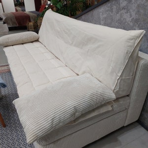 May include: A cream-colored sofa with corduroy fabric and a quilted seat. The sofa has a large back cushion and two corduroy pillows. The sofa is in a showroom setting.