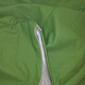 May include: Close-up of a green fabric with a zipper detail. The zipper is partially open, revealing a light-colored interior. The fabric appears to be a durable material, possibly for a bag or cushion cover.