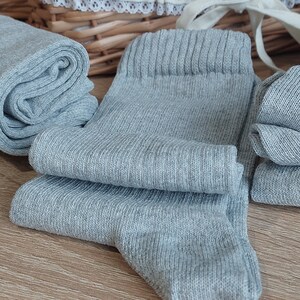May include: A set of gray socks made of a soft, knitted fabric. The socks are folded and stacked on a wooden surface.