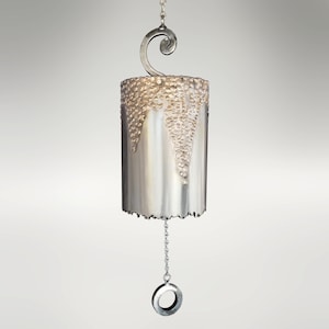 May include: A silver metal wind chime with a textured surface and a decorative swirl at the top. The chime hangs from a chain with a ring at the bottom.