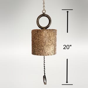 May include: A gold-colored metal wind chime with a textured surface hangs from a chain. The chime is 20 inches long and has a circular top.