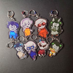 Puede incluir: Ocho llaveros de personajes de dibujos animados coloridos con signos de paz. Los personajes están en llaveros de acrílico transparente con anillos de llaves plateados.