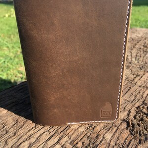 May include: A brown leather notebook with white stitching and a small logo embossed on the front.