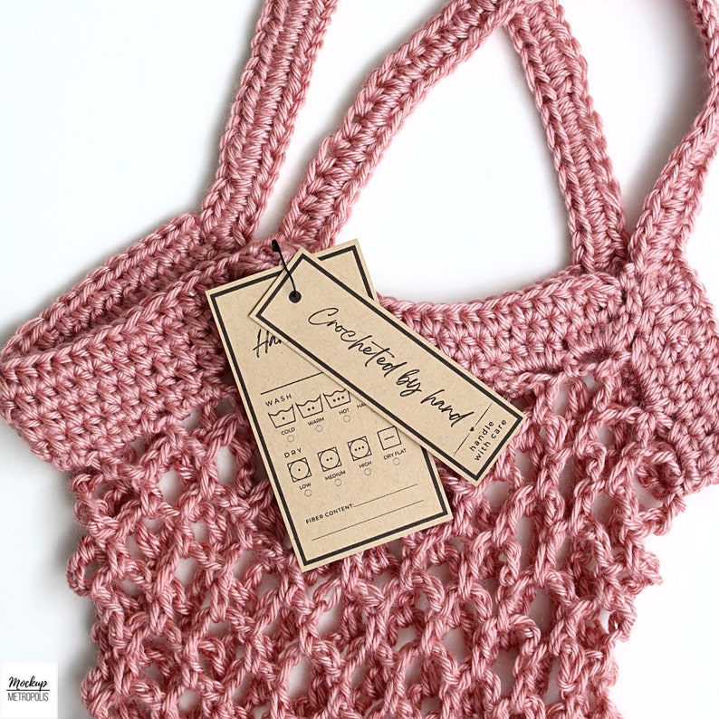 K&ouml;nnte beinhalten: Eine rosa geh&auml;kelte Tasche mit einem braunen Papieretikett, auf dem "Crocheted bag find" steht und Pflegehinweise enthalten sind. Das Etikett tr&auml;gt au&szlig;erdem den Hinweis "Handle with care".