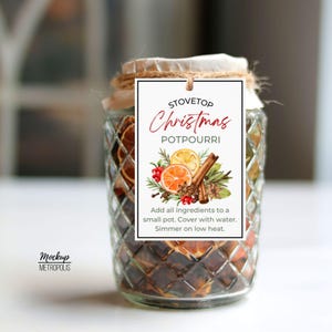 Könnte beinhalten: Ein klares Glas mit Rautenmuster, gefüllt mit getrockneten Früchten und Gewürzen. Ein weißes, rechteckiges Etikett ist mit einer Schnur am Deckel befestigt und zeigt den Text STOVETOP Christmas POTPOURRI, eine botanische Illustration und Anweisungen.