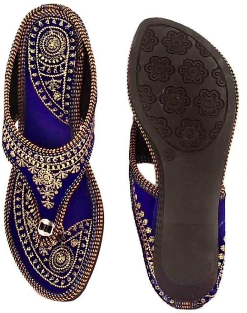 May include: A pair of blue and gold embroidered sandals. The sandals feature intricate gold threadwork on a blue velvet base. The soles are dark brown with a floral pattern. The sandals are designed with a toe loop and ankle strap.
